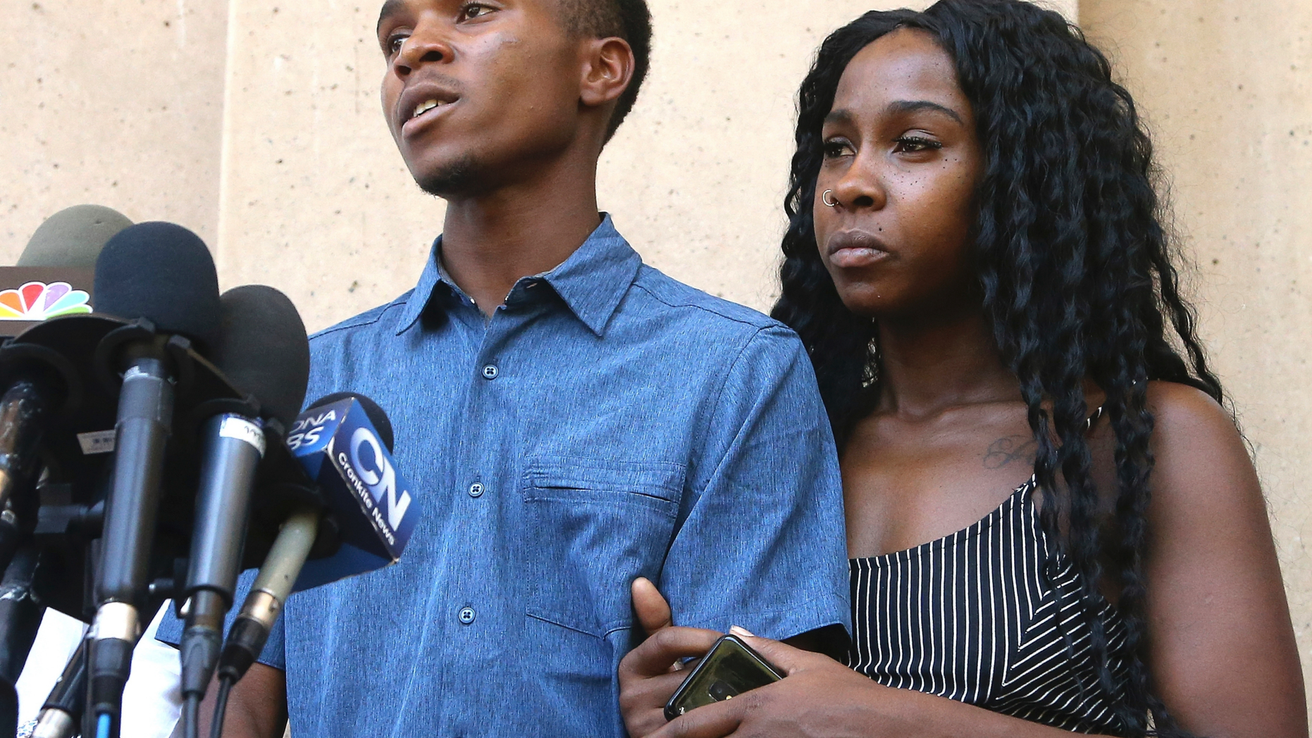 Dravon Ames, left, answers a question as Iesha Harper, right, joins her fiancee during a news conference at Phoenix City Hall, Monday, June 17, 2019, in Phoenix. Ames and his pregnant fiancée, Harper, who had guns aimed at them by Phoenix police during a response to a shoplifting report, say they don't accept the apologies of the city's police chief and mayor and want the officers involved to be fired. (AP Photo/Ross D. Franklin)