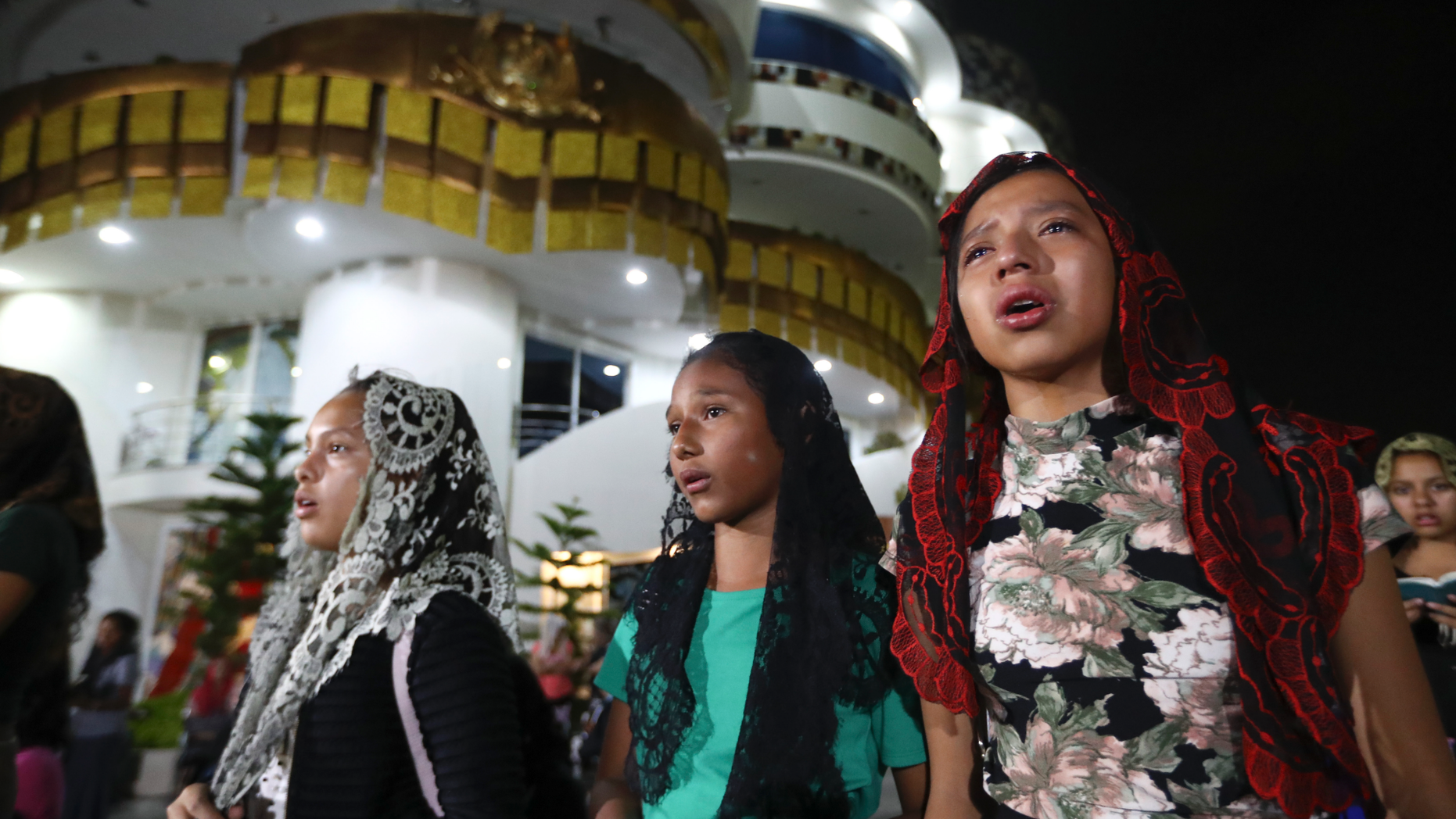 Young women pray outside the "La Luz Del Mundo" or Light of the World church after members learned their church's leader Joaquin Garcia was arrested in the U.S., in Guadalajara, Mexico, Tuesday, June 4, 2019. California authorities have charged Garcia, the self-proclaimed apostle of the Mexico-based church that claims over 1 million followers, with child rape, human trafficking and producing child pornography in Southern California. (AP Photo/Refugio Ruiz)