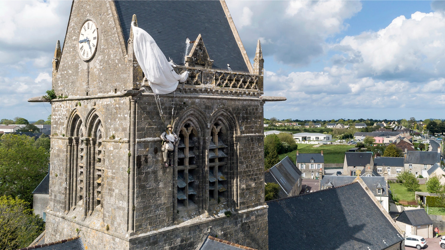 In this photo taken with a drone, a dummy paratrooper representing a WWII paratrooper from the 82nd Airborne hangs on the bell tower of the church of Sainte Mere Eglise, in Normandy, France, Thursday, May 9, 2019. Seventy-five years ago, American paratrooper John Steele dangled from a clock tower in Sainte-Mere-Eglise after his parachute got caught during the D-Day invasion, and survived. (AP Photo/David Vincent)
