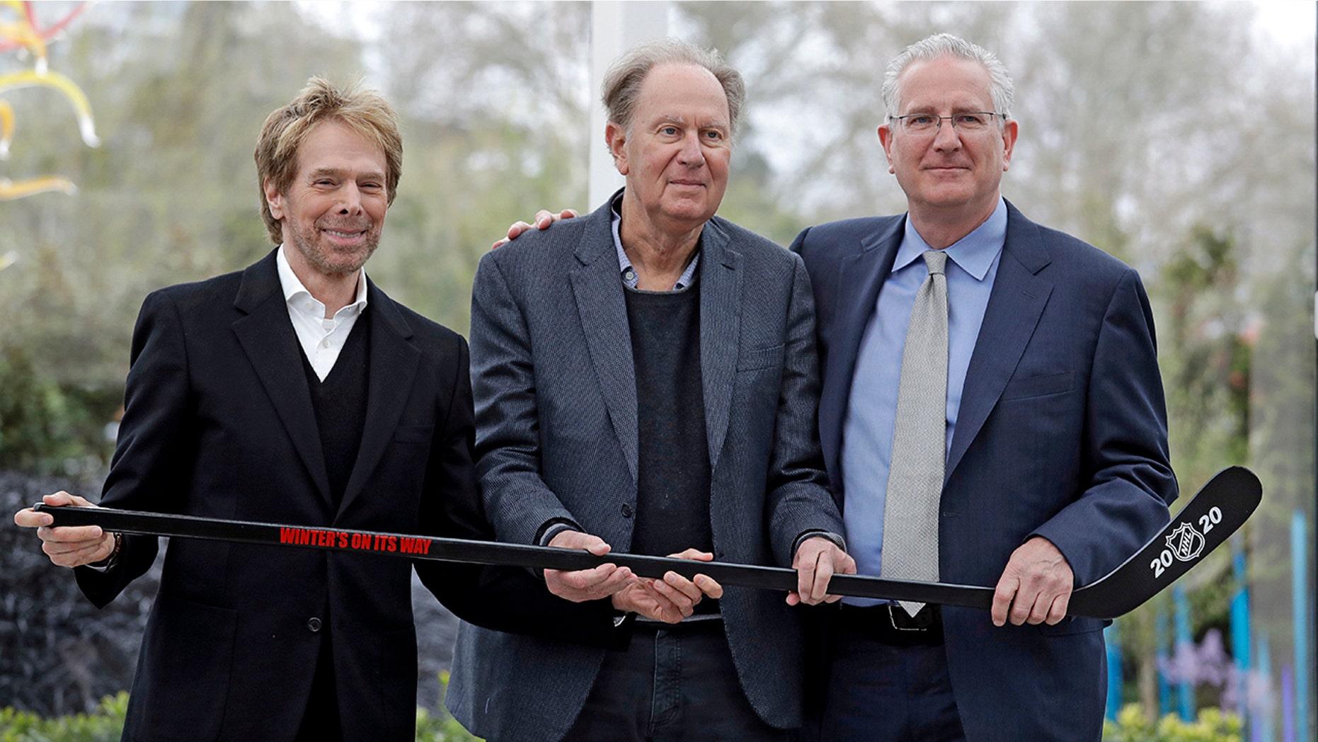 FILE - In this April 11, 2018, file photo, part-owners, from left to right, Jerry Bruckheimer and David Bonderman pose with Tod Leiweke and a hockey stick during a news conference naming Leiweke as the president and CEO for a prospective NHL expansion team in Seattle. (AP Photo/Elaine Thompson, File)