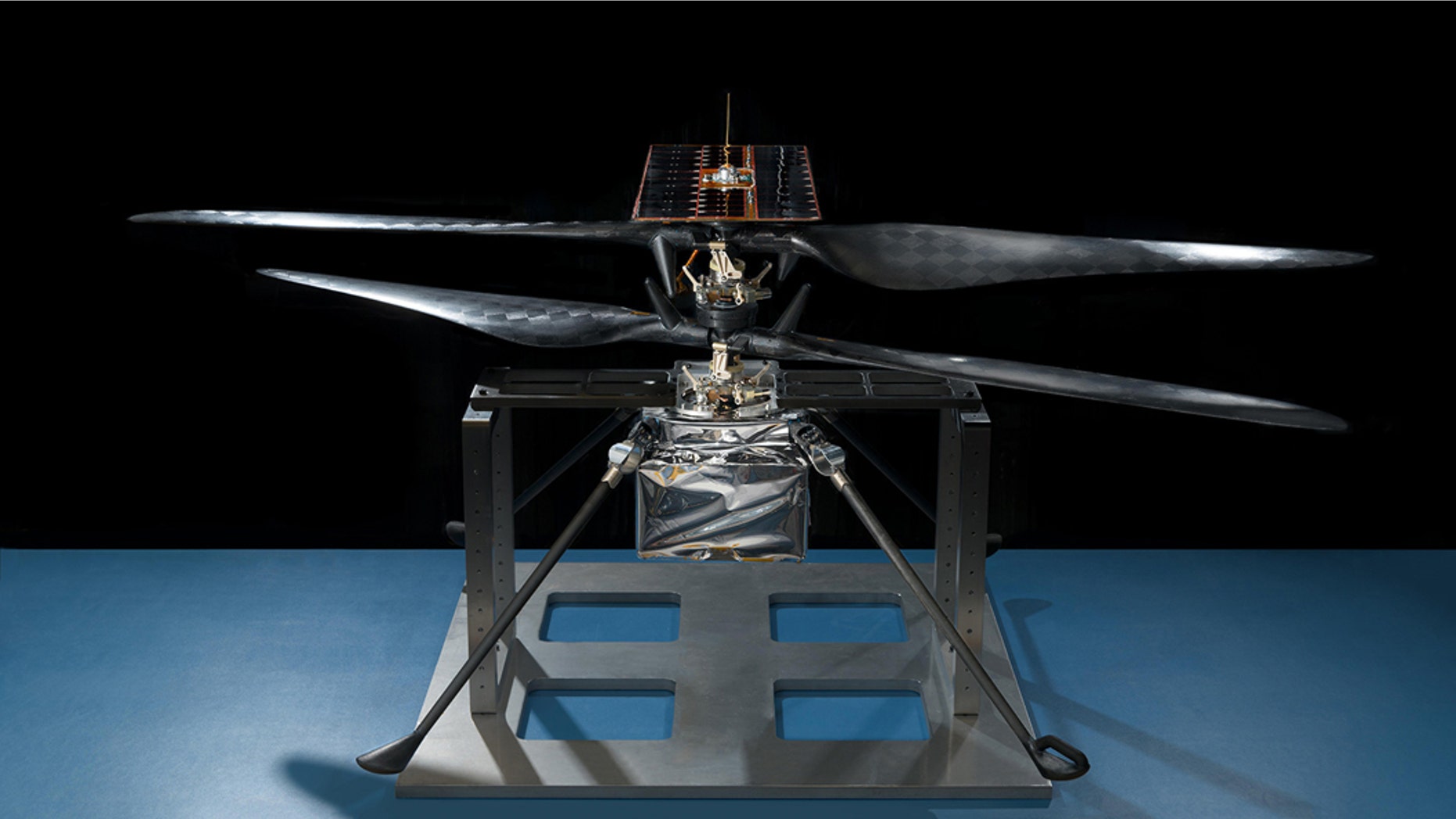 This image of the flight model of NASA's Mars Helicopter was taken on Feb. 14, 2019, in a cleanroom at NASA's Jet Propulsion Laboratory in Pasadena, California. The aluminum base plate, side posts, and crossbeam around the helicopter protect the helicopter's landing legs and the attachment points that will hold it to the belly of the Mars 2020 rover. (Credit: NASA/JPL-Caltech )