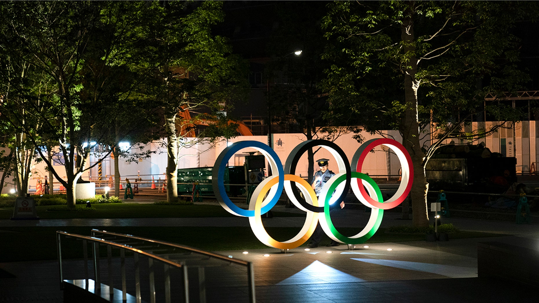 In this June 23, 2019, photo, a security officer uses a flashlight to check on the Olympic Rings in front of the New National Stadium in Tokyo. Overwhelmed by unprecedented demand, Tokyo Olympic organizers said Thursday they would run another ticket lottery next month for residents of Japan to view the games. Millions of Japanese were let down last month when they came away empty-handed without tickets for next year's Olympics. (AP Photo/Jae C. Hong)