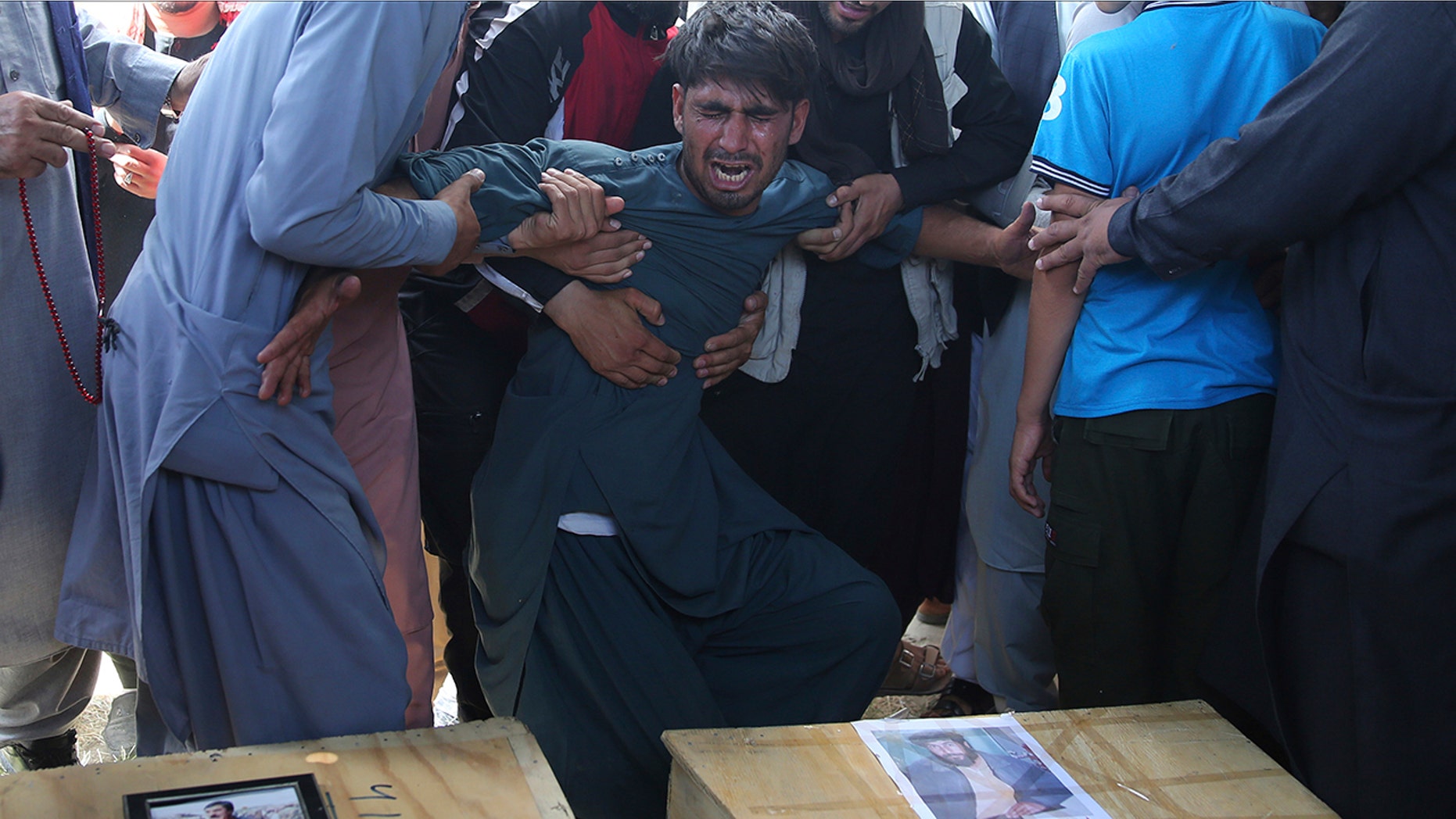 A relative wails near the coffins of victims of the Dubai City wedding hall bombing during a mass funeral in Kabul, Afghanistan. (AP Photo/Rafiq Maqbool)