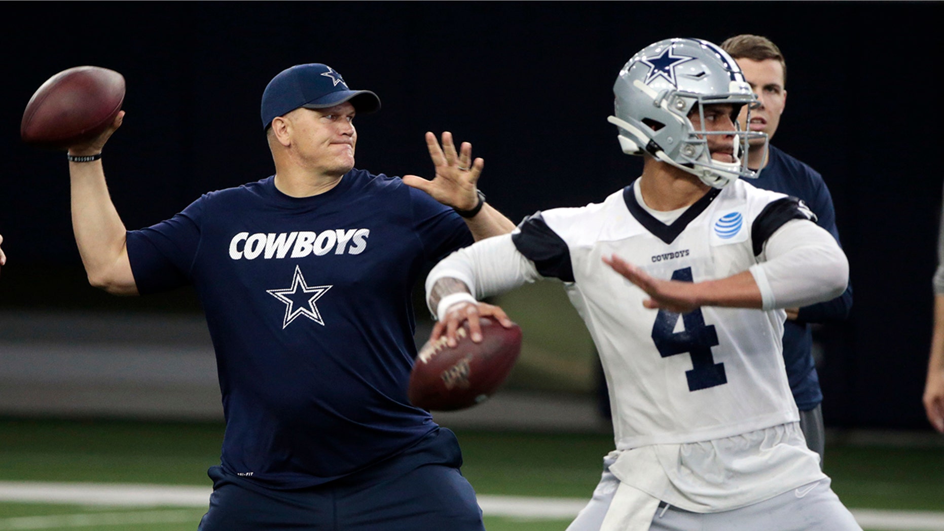 FILE - In this Wednesday, May 22, 2019 file photo, Dallas Cowboys quarterbacks coach Jon Kitna throws the ball alongside Dak Prescott (4) during NFL football practice in Frisco, Texas. Jon Kitna is back in the NFL with one of the quarterback’s former teams in the Dallas Cowboys after coaching high school football for seven years. Kitna’s return has plenty to do with his strong relationship with coach Jason Garrett. (AP Photo/Michael Ainsworth, File)