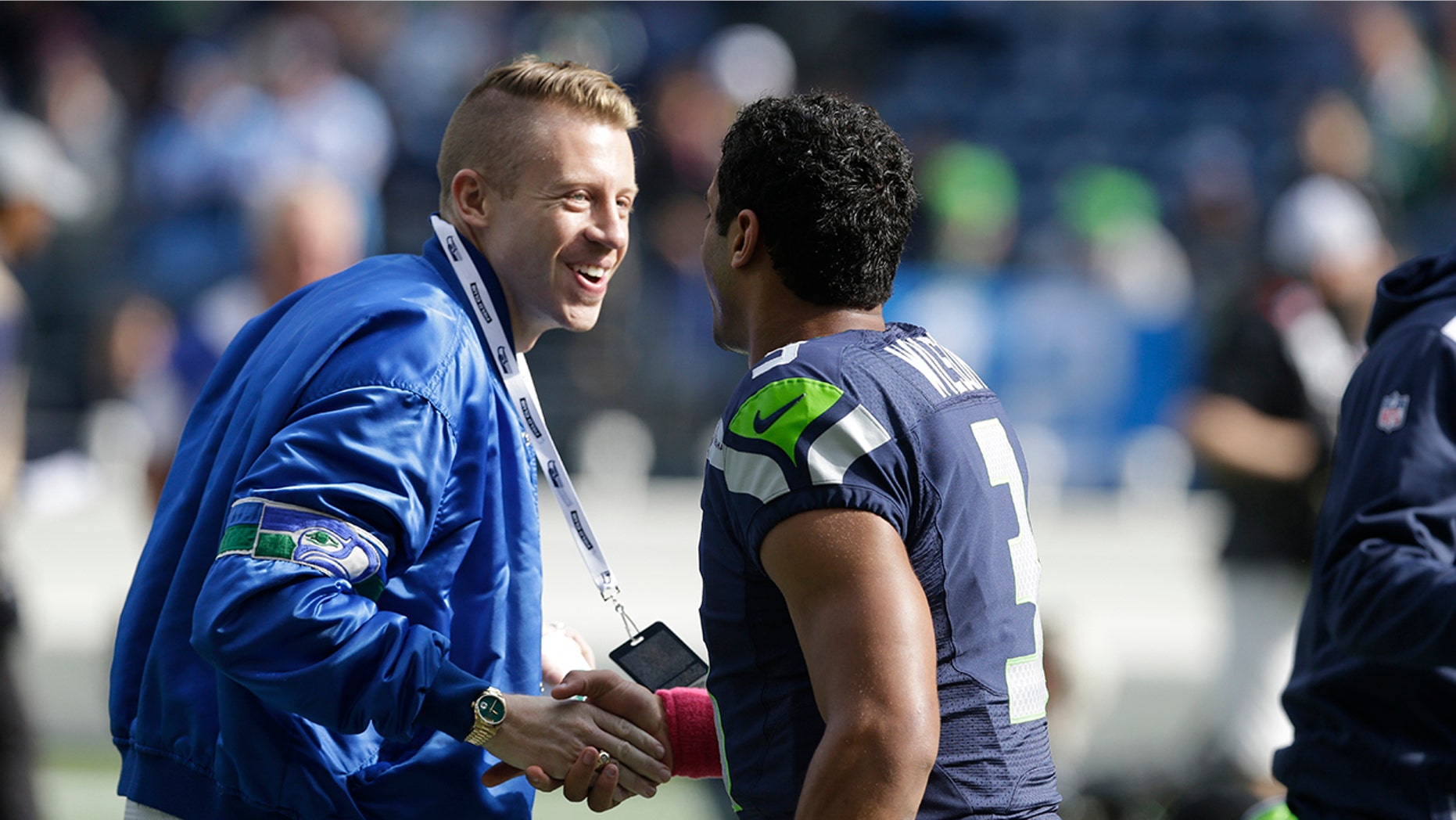 FILE - In this Oct. 13, 2013, file photo, Seattle hip hop and rap singer Macklemore, left, greets Seattle Seahawks quarterback Russell Wilson before an NFL football game between the Seahawks and Tennessee Titans in Seattle. The MLS soccer Seattle Sounders team announced Tuesday, Aug. 13, 2019, that they are adding Macklemore and Wilson to club's ownership group, along with several others as Hollywood producer Joe Roth leaves the franchise.(AP Photo/Elaine Thompson, File)