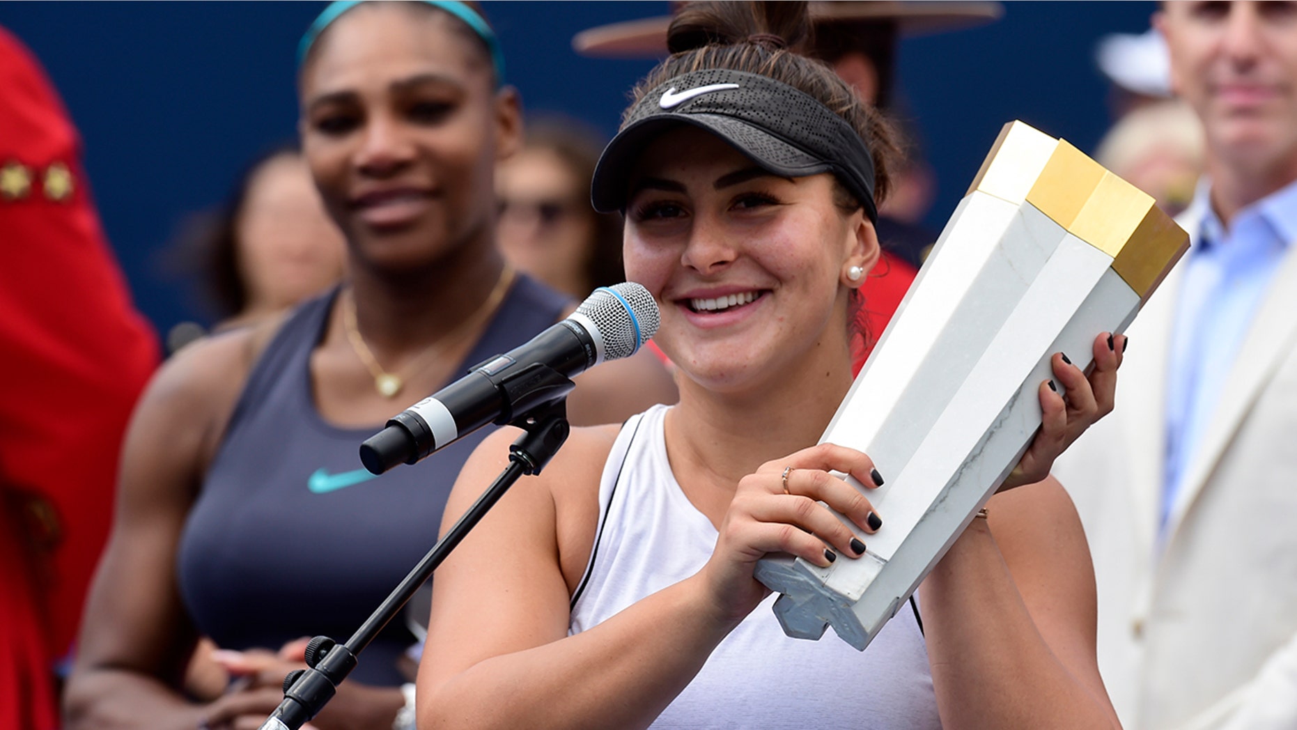 Canada's Bianca Andreescu holds the winner's trophy as Serena Williams of the USA looks on after Williams had to retire from the final of the Rogers Cup tennis tournament in Toronto on Sunday, Aug. 11, 2019. (Frank Gunn/The Canadian Press via AP)