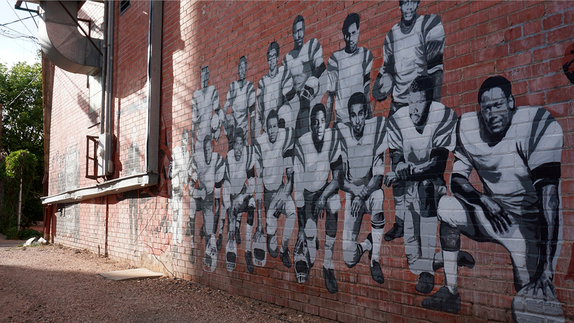 In this Wednesday, Sept. 11, 2019 photo shows part of an alleyway mural in downtown Laramie, Wyo., that honors the Black 14. The Black 14 were black athletes dismissed from the University of Wyoming football team in 1969 for seeking to protest racism by wearing black armbands in a game against Brigham Young University. The university plans to dedicate a plaque honoring the group at War Memorial Stadium on Friday. (AP Photo/Mead Gruver)
