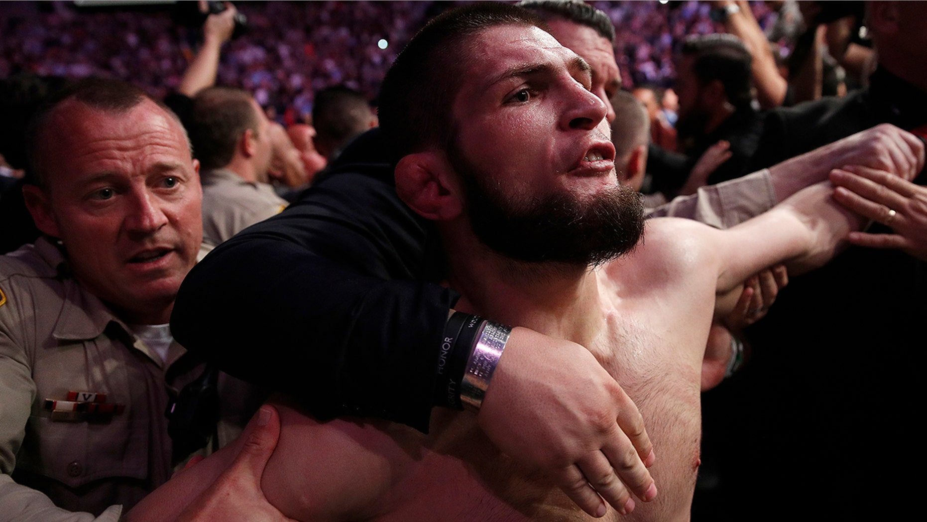 FILE - In this Oct. 6, 2018, file photo, Khabib Nurmagomedov is held back outside of the cage after fighting Conor McGregor in a lightweight title mixed martial arts bout at UFC 229 in Las Vegas. Nurmagomedov has not fought in the 11 months since he punctuated his star-making victory over McGregor at UFC 229 in Las Vegas by scaling the fence and jumping into the crowd to fight McGregor’s entourage. (AP Photo/John Locher, File)