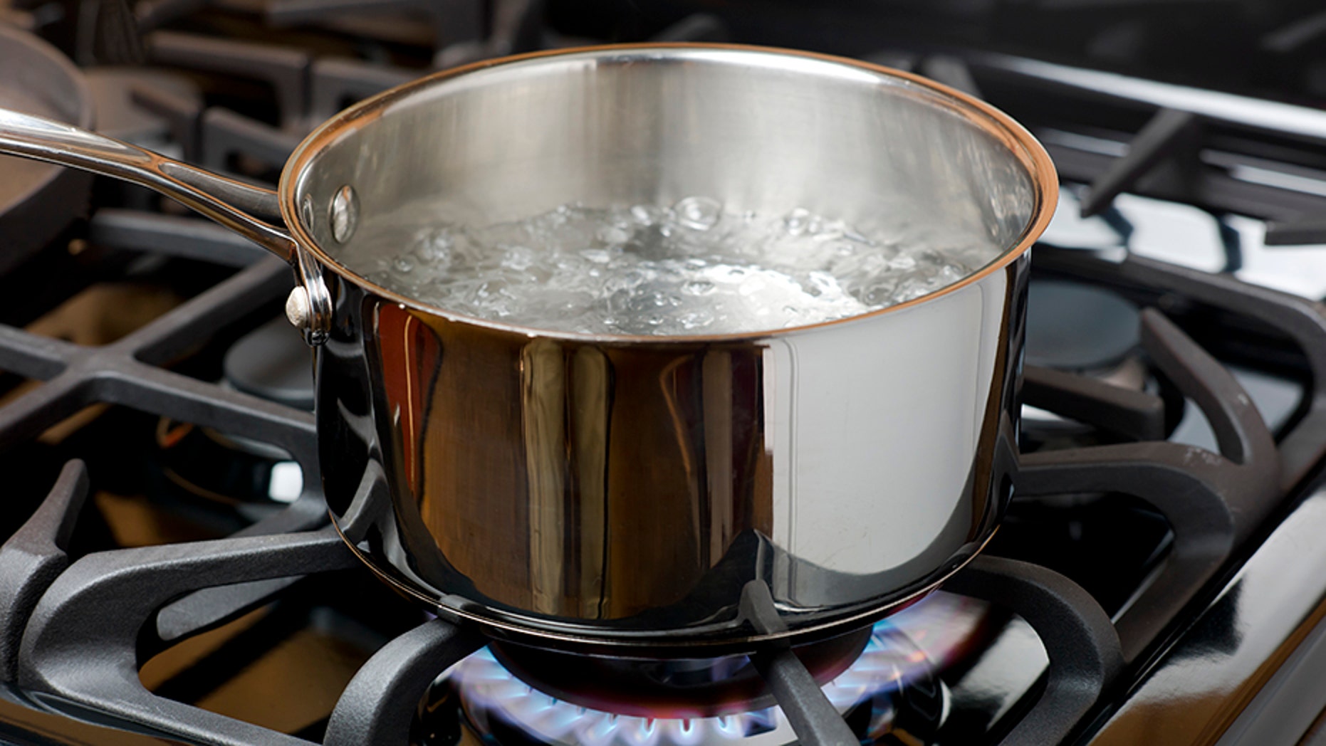 Water bubbles and boils on a gas stove or range in a home kitchen. Blue flame and stainless steel pot.