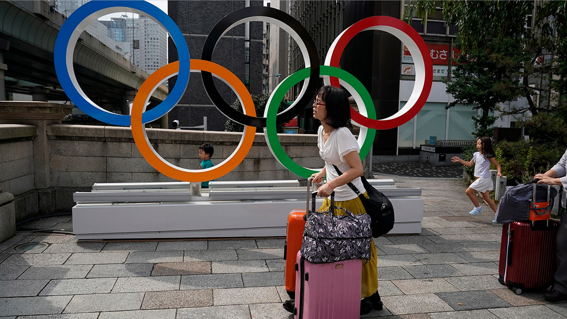 FILE - In this Aug. 19, 2019, file photo, tourists walk with their luggage past the Olympic rings in Tokyo. Frustrated residents of Japan got another shot at attending next year’s Tokyo Olympics when organizers on Friday, Nov. 8, 2019, put about 1 million more tickets into the latest lottery. (AP Photo/Jae C. Hong, File)