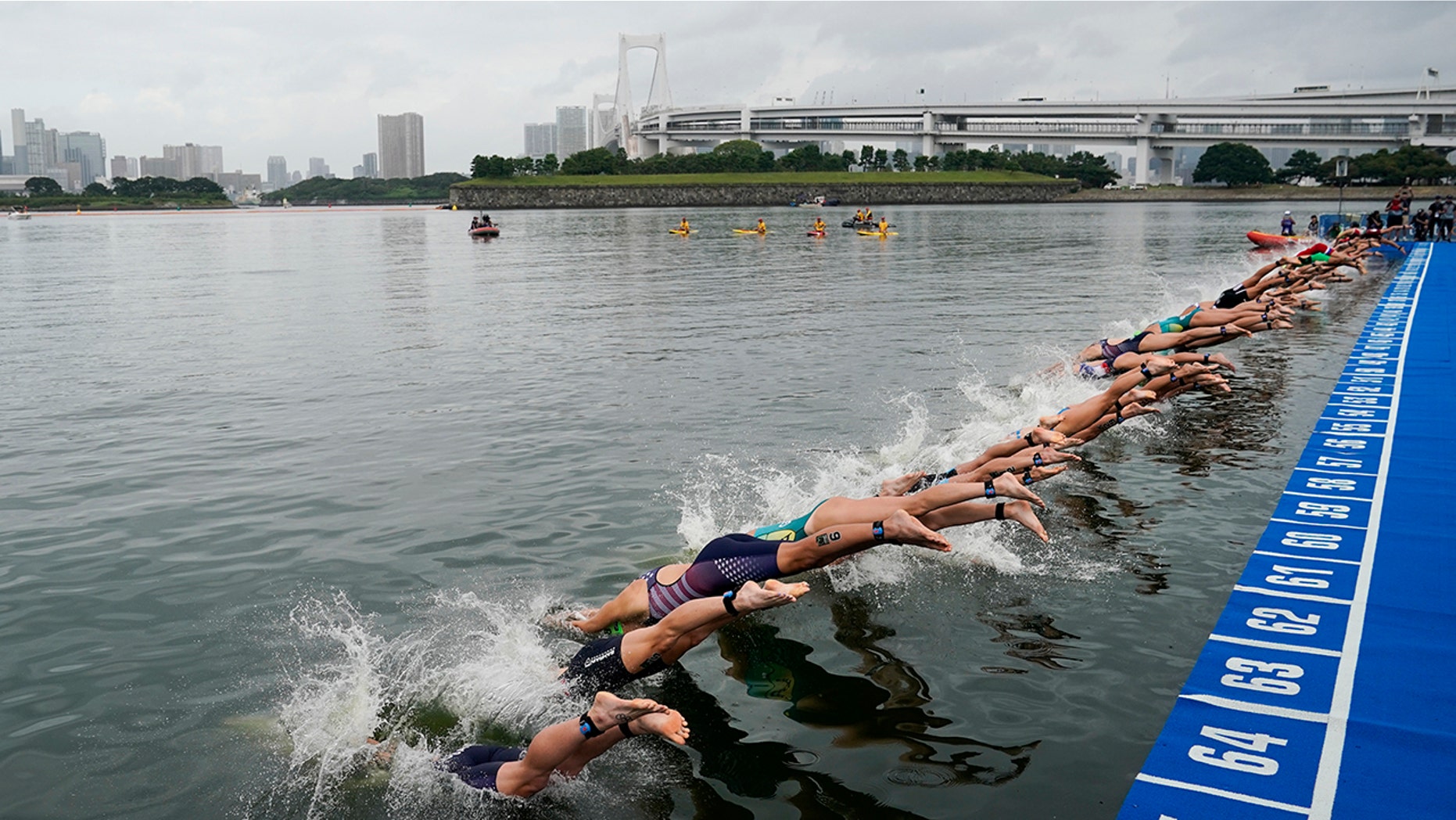 FILE - In this Aug. 15, 2019, file photo, athletes dive into the water at the start line during a women's triathlon test event at Odaiba Marine Park, a venue for marathon swimming and triathlon at the Tokyo 2020 Olympics, in Tokyo. The IOC moved next year’s Tokyo Olympic marathons and race walks out of the Japanese capital to avoid the stifling heat and humidity. Some swimmers and an 11,000-member coaching body want similar treatment: find an alternative to the distance-swimming venue in Tokyo Bay known as the “Odaiba Marine Park.”(AP Photo/Jae C. Hong, File)