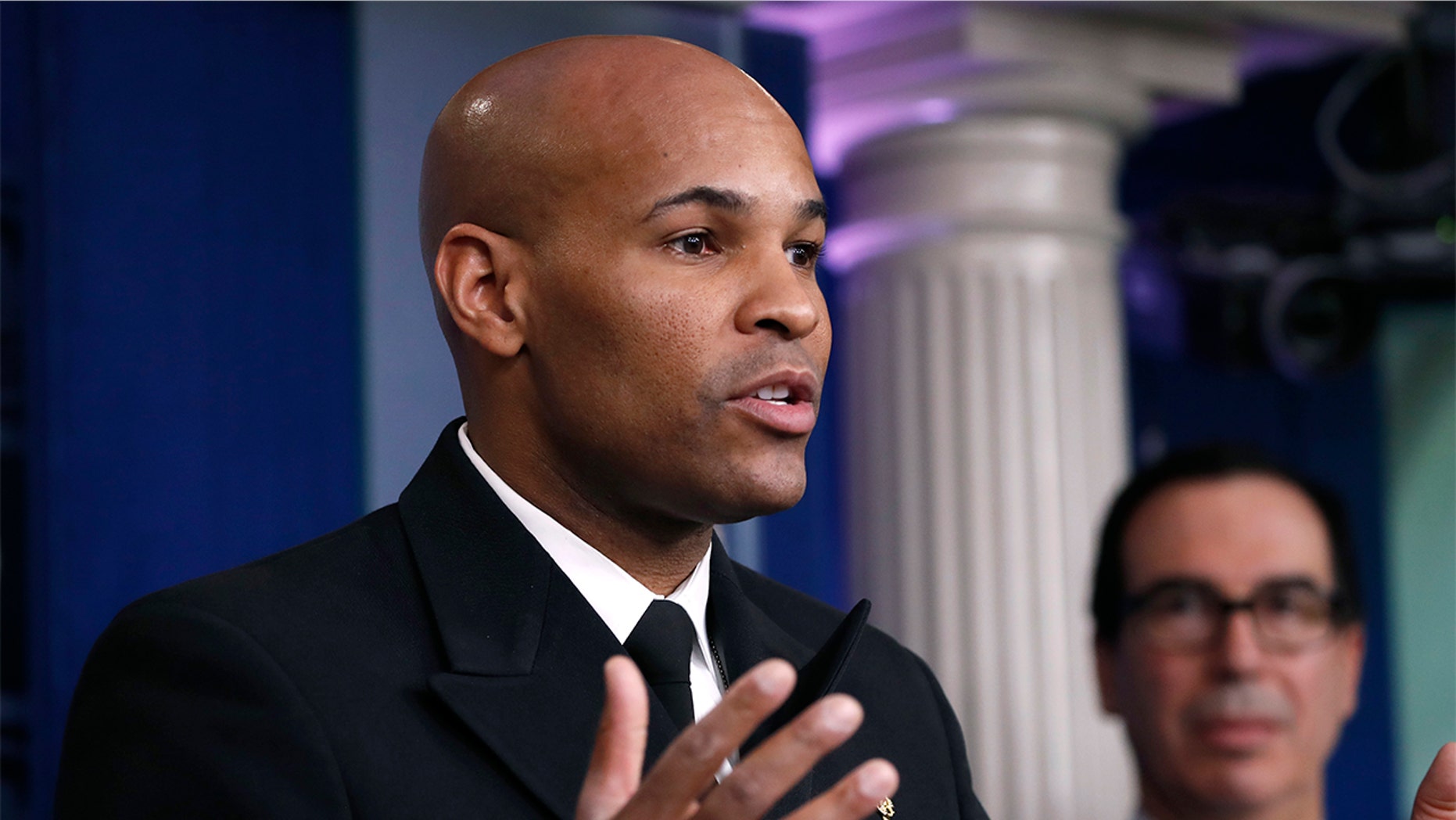 U.S. Surgeon General Jerome Adams speaks during a briefing on coronavirus in the Brady press briefing room at the White House, Saturday, March 14, 2020, in Washington, as Treasury Secretary Steven Mnuchin listens. (AP Photo/Alex Brandon)