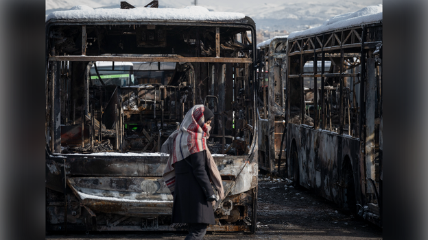 An unidentified woman walks past the burned buses on January 21, 2026, that were set ablaze during anti-regime protests.