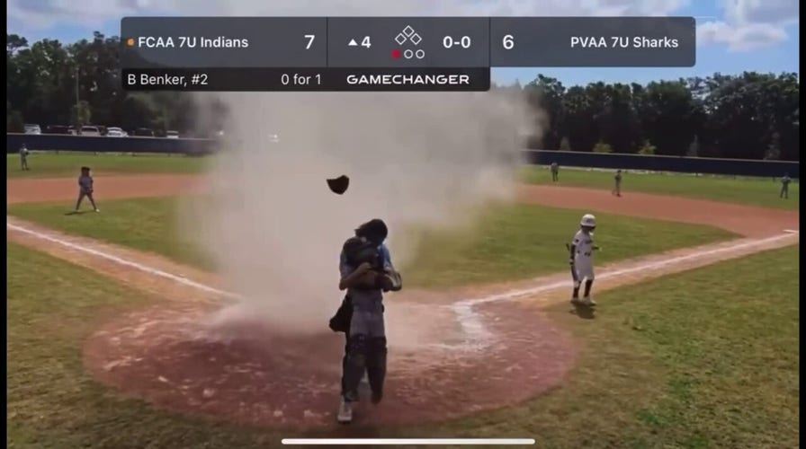 Umpire shields child from dust devil during youth baseball game