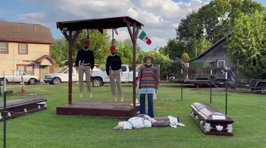 Houston Halloween display shows mannequins in red hats hanging from gallows with Mexican flag