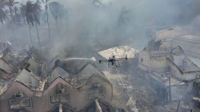 A drone sprays smoldering buildings with water after a fire blazed the Dominican resort town Bayahibe