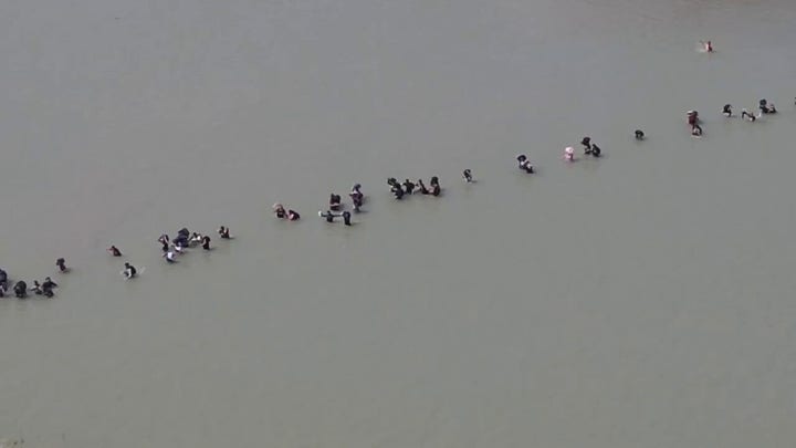 Aerial footage shows a large group of migrants wading in water to cross the US-Mexico border