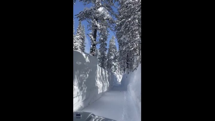 A car drives between towering walls of snow to reach California property after storm