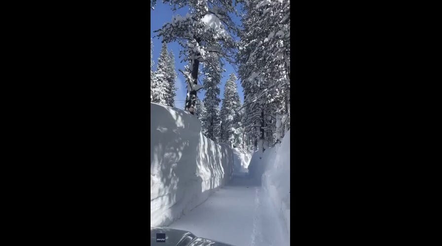 A car drives between towering walls of snow to reach California property after storm