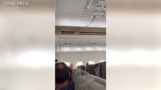 Passengers scramble to protect themselves as water flows down into airline cabin