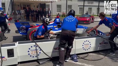 An INDYCAR driver zooms towards pit crew at preview of America 250 Grand Prix.