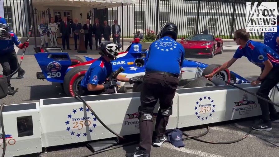 An INDYCAR driver zooms towards pit crew at preview of America 250 Grand Prix.