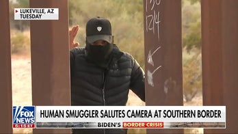 Smuggler salutes camera as he leads migrants through broken section of border wall