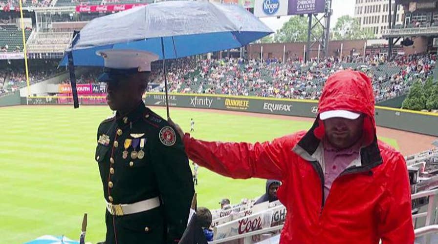 Baseball fan holds an umbrella over a JROTC cadet