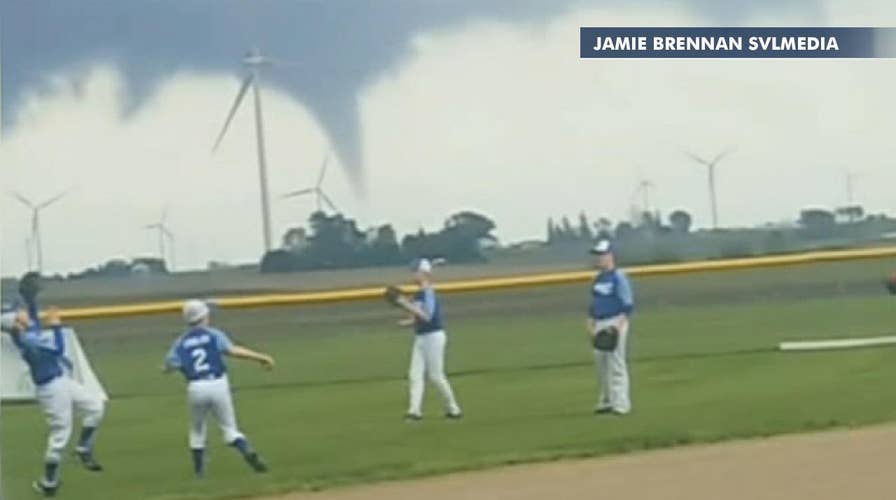 Baseball team practices with a tornado visible in the distance