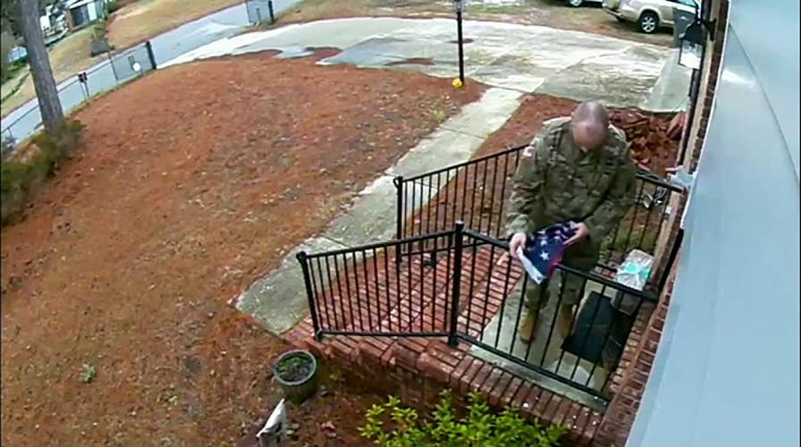 Man in military uniform folds flag torn from pole during a storm, returns it to owners' porch