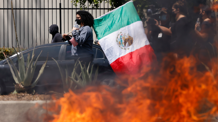 Masked protester with flag standing near flames - Fox News