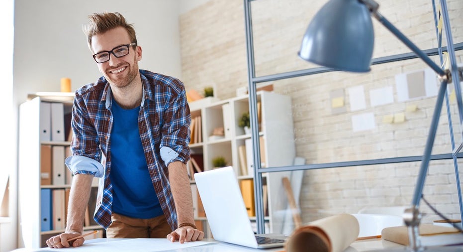 Happy young employee standing by workplace in office