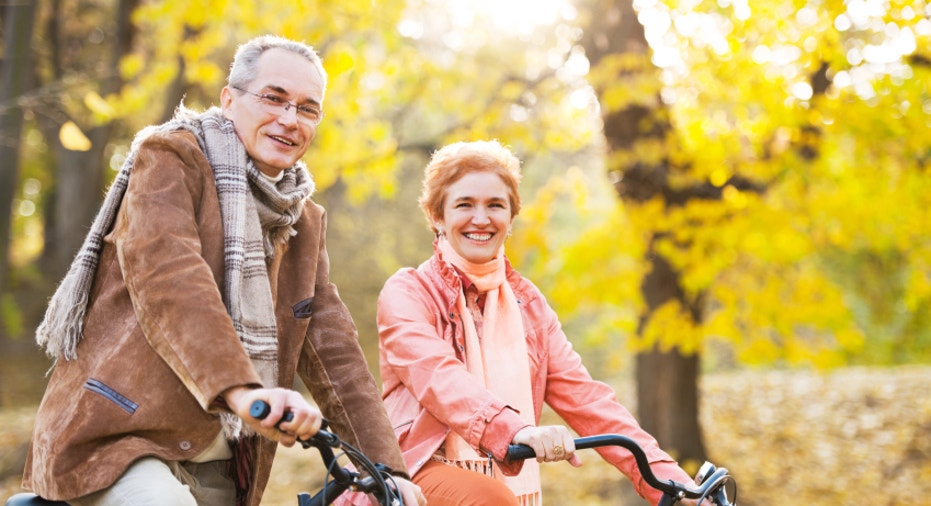 Mature adult couple riding bicycles in park.