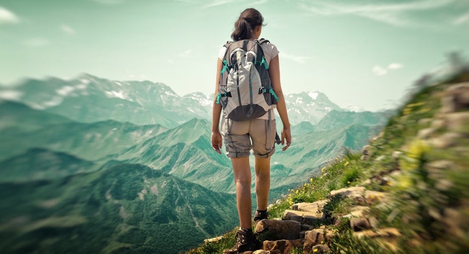 Woman hiking in mountain range. Rear view of a female backpacker walking on a small foot path in a m