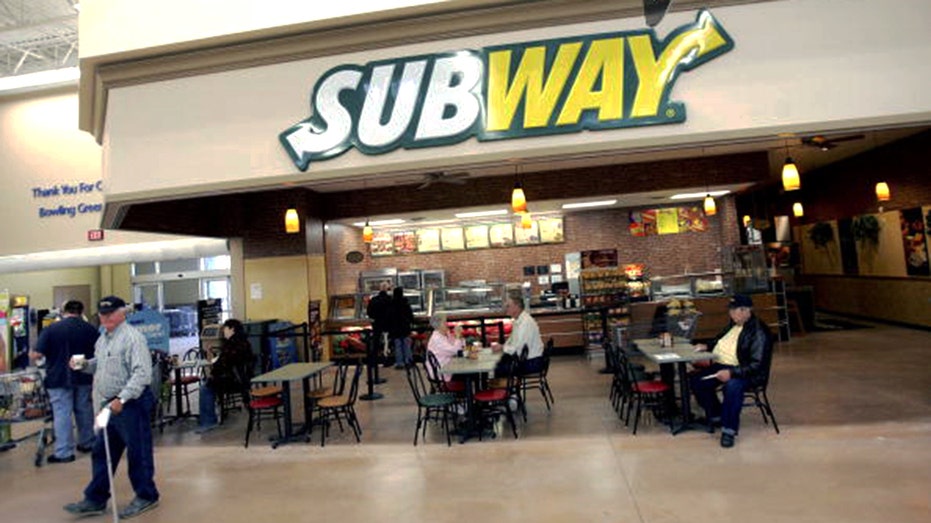 A Subway shop with people sitting and eating out front