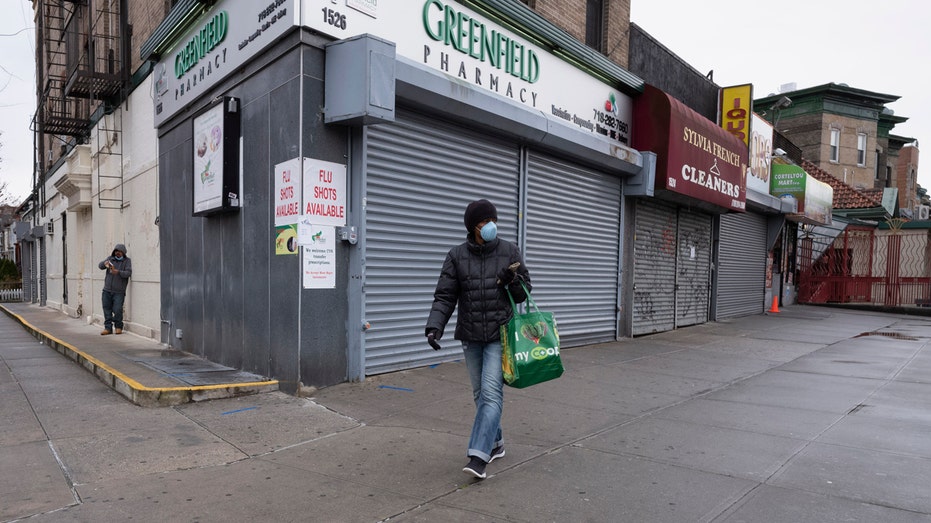 Pictured this Friday, April 3, 2020, a woman walks past local stores during a coronavirus pandemic in New York City. 