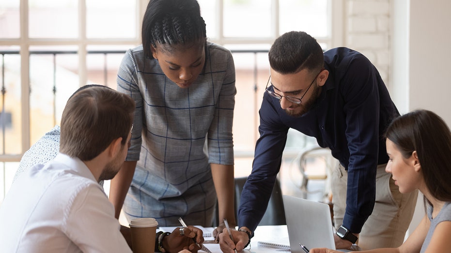 Workers in office huddle together to work on project