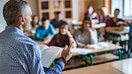 Rear view of male professor teaching a lecture to high school students in the classroom.