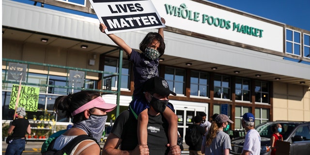 CAMBRIDGE - JULY 18: A child holds a Black Lives Matter sign in front of Whole Foods Market while supporting workers who walked out in solidarity after getting dismissed from Whole Foods for wearing Black Lives Matter face masks in Cambridge, MA on July 18, 2020. (Photo by Erin Clark/The Boston Globe via Getty Images)