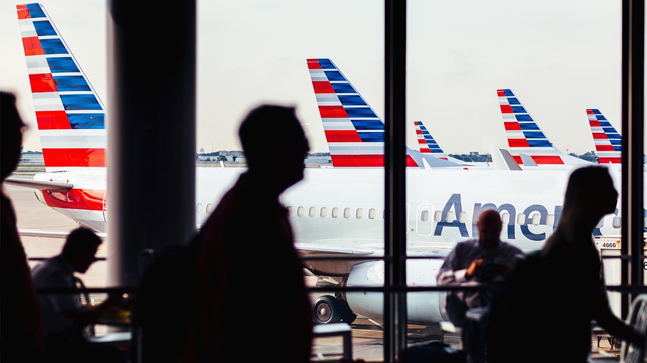 Individuals walking in airport with American airplanes behind