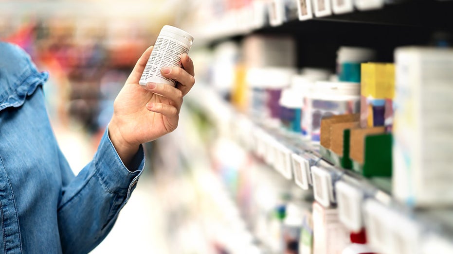 person holding bottle of prescription drugs near pharmacy shelf