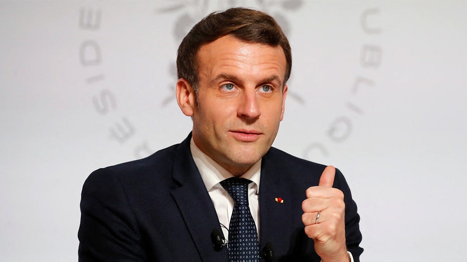 Emmanuel Macron makes a thumbs up gesture in a suit
