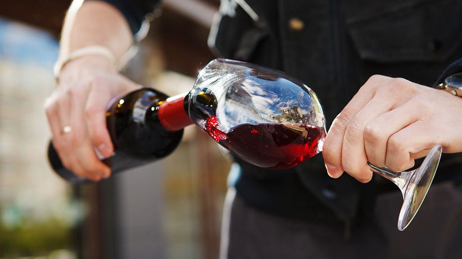 Man pouring wine into wineglass, male hand holding bottle