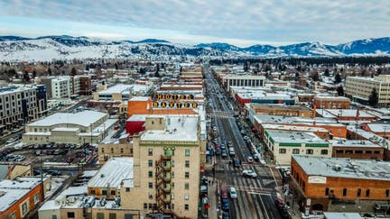 Aerial View of Main Street in downtown Bozeman Montana. Winter snow is scattered on streets and buildings with the mountain range covered in snow in the distance. Famous Baxter Hotel Sign is seen up close.