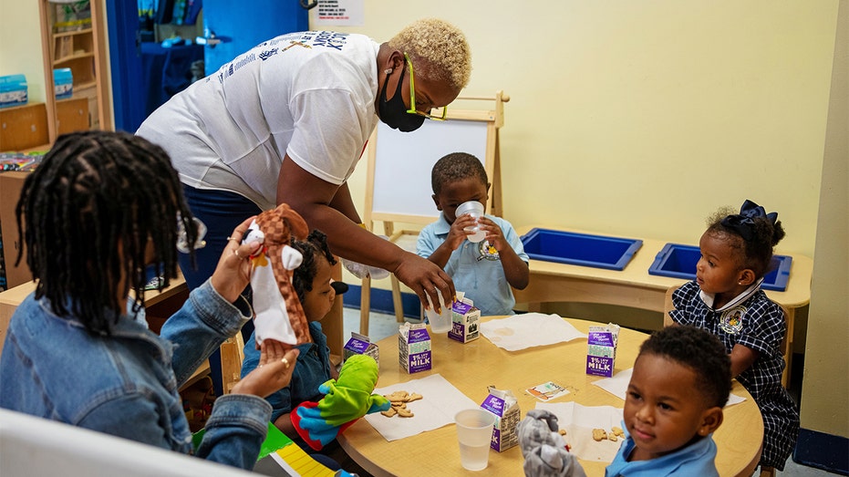 Rochelle Wilcox delivers cartons of milk to the 2-year-olds classroom as teacher Steneisha Morehead sits at left with students Andrew Robair III, Amore Smalls, Roemello Jones and King Adams at Wilcox's Academy of Early Learning in New Orleans, Louisiana, Aug. 24, 2021. 