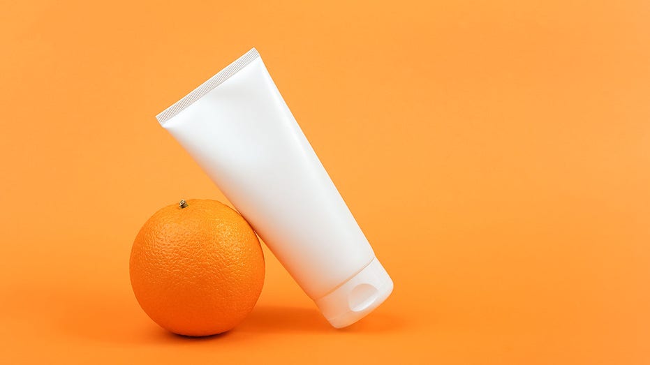White blank cosmetic bottle, tube of cream, lotion for body, face or hand, orange fruit. Concept cosmetics with vitamin C, antioxidants or anti-cellulite. Mockup Front view Copy space