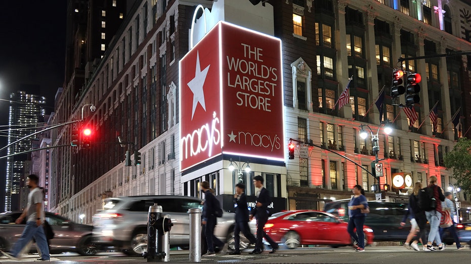 People walk past large Macy's billboard on a building in front of Macy's Herald Square store