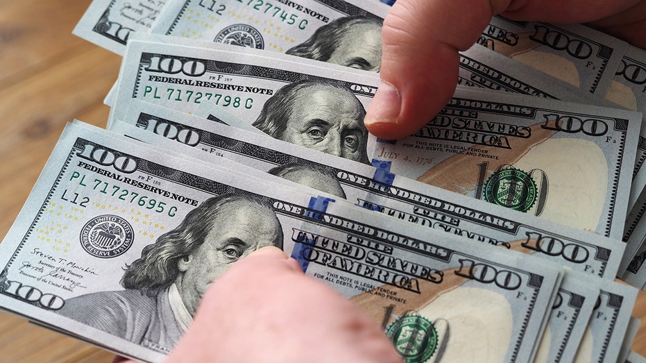In this photo illustration, hands count U.S. $100 bills. 