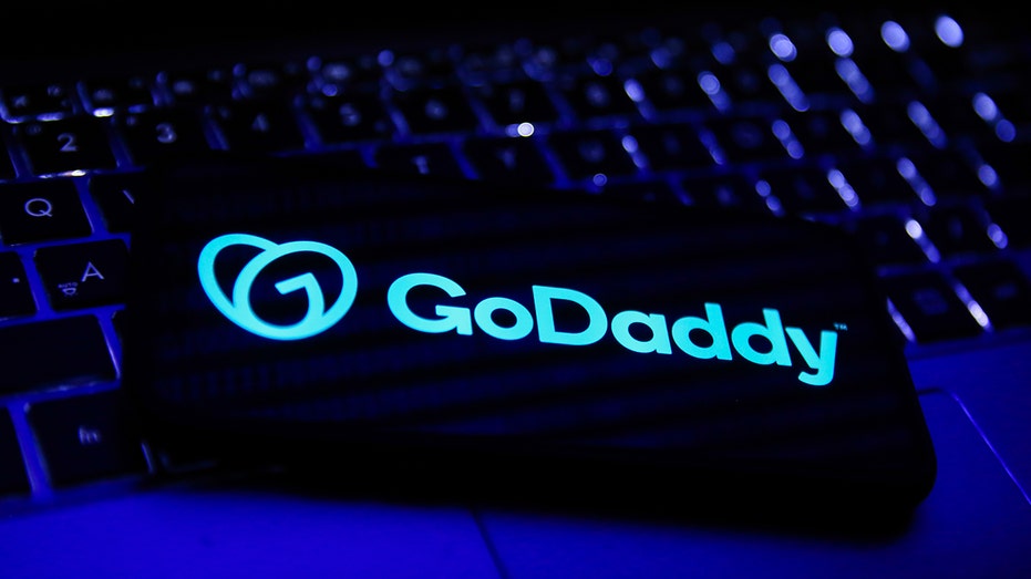 GoDaddy logo displayed on a phone screen and a laptop keyboard in this illustration photo taken in Krakow, Poland, on Nov. 22, 2021.