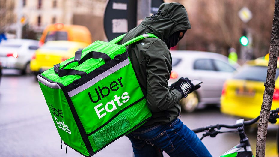 Young man on a bike with Uber Eats logo delivering food during a rainy day in Bucharest, Romania, 2020